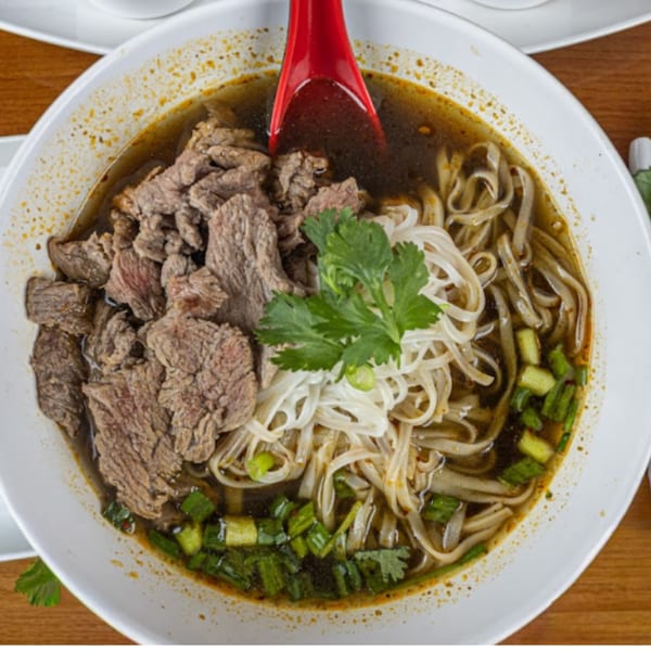 Close-up of Thai beef noodle soup with cilantro, green onions, and a red spoon.