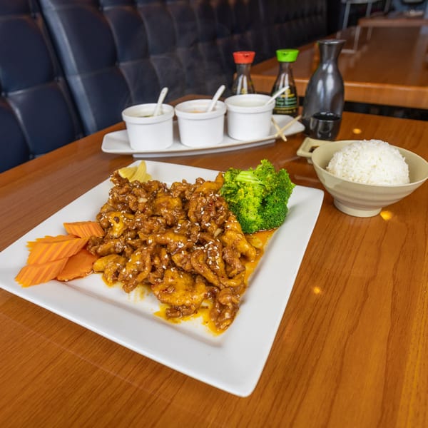 Thai Spice Lees Summit's orange chicken with broccoli, carrots, and rice on a wooden table.