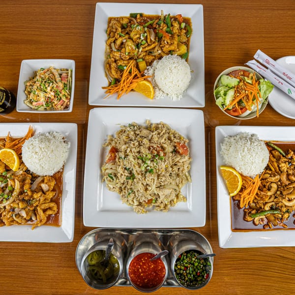 Overhead view of a Thai feast with multiple entrees, fried rice, salads, and condiments on a wooden table.