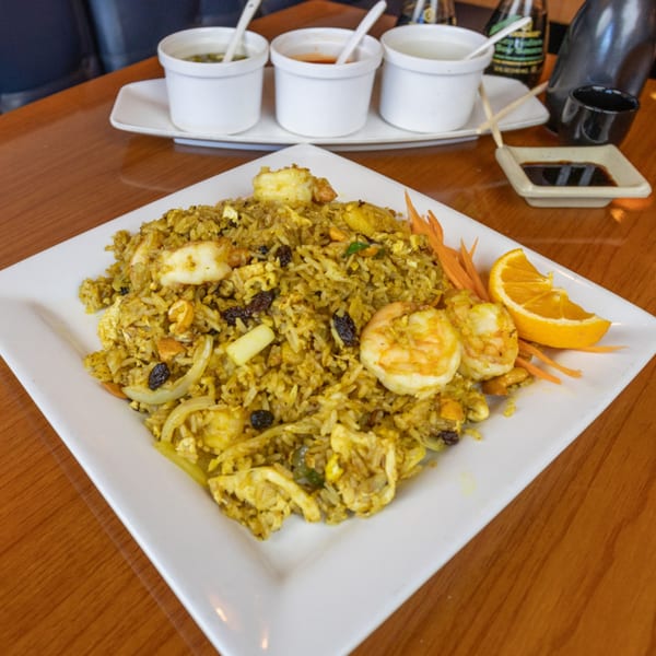 Curry fried rice with shrimp, squid, raisins, and cashews, garnished with an orange slice.