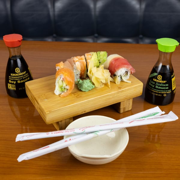 Assorted sushi rolls, wasabi, and pickled ginger on a wooden board with soy sauce bottles.