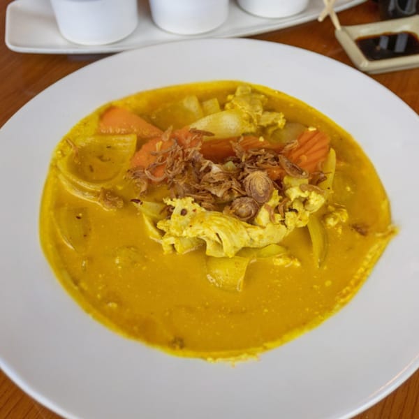 A vibrant yellow Thai curry with chicken, carrots, and fried shallots in a white bowl.
