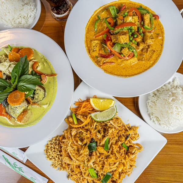 Overhead view of Thai green curry, red curry, Pad Thai, and white rice on a wooden table.