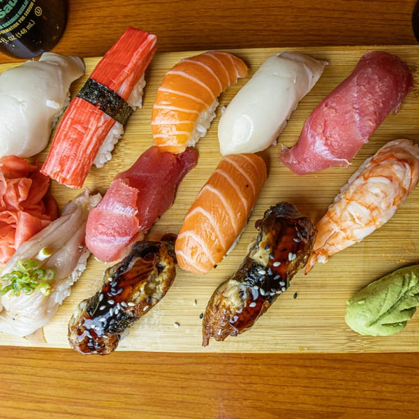 Assortment of colorful sushi and sashimi, including salmon, tuna, shrimp, and eel, on a wooden board.