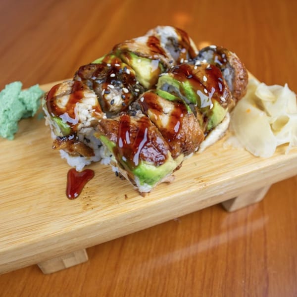 Dragon roll sushi with eel, avocado, sesame seeds, and sweet sauce, served with wasabi and ginger.